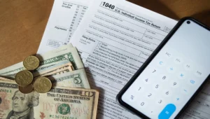 IRS Form 1040 with US dollar bills, coins, and a smartphone calculator for estimated tax payments