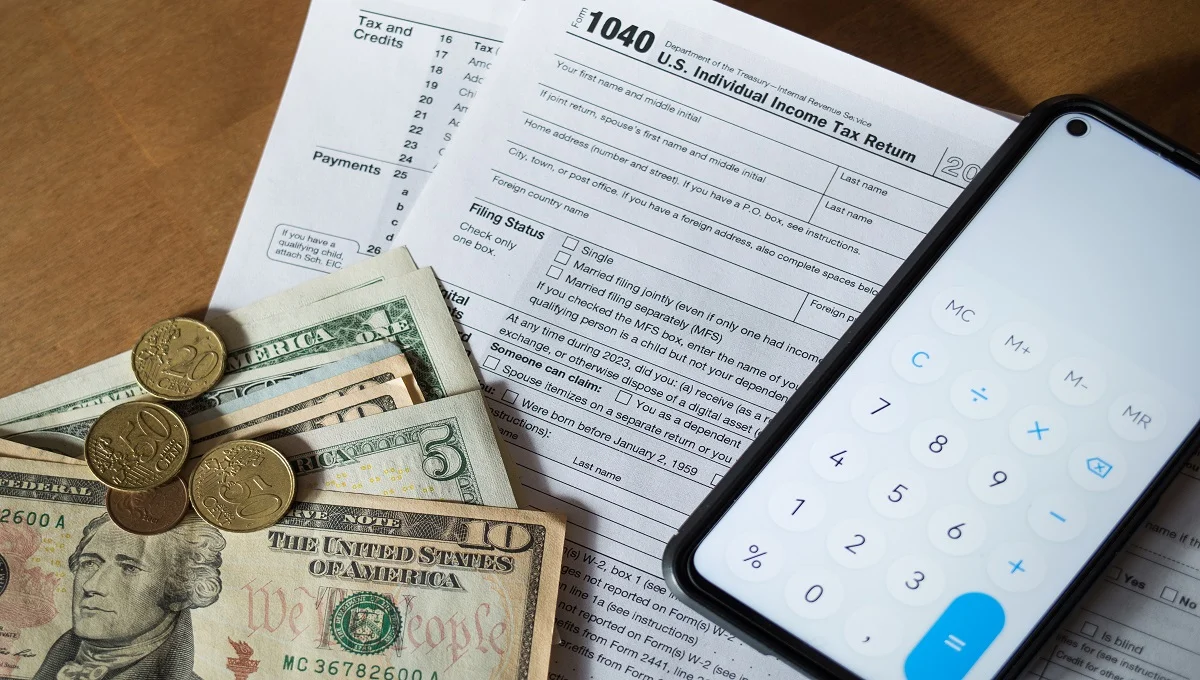 IRS Form 1040 with US dollar bills, coins, and a smartphone calculator for estimated tax payments